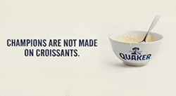 Bowl of porridge with Quaker Oats logo on it and spoon inside on a white background. Text above the bowl reads Champions are not made on croissants.